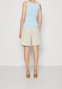 Débardeur côtelé bleu clair associé à un short en lin beige. Le short présente une coupe ample et droite, complétée par des sandales à talons.