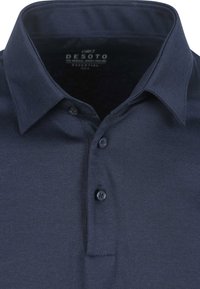 Donkerblauwe polo met een gestructureerde stof, een knoopsluiting met drie knopen en een nette kraag. Merktag zichtbaar aan de binnenkant van de kraag.