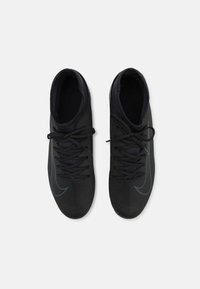 Des chaussures de sport noires avec une tige en maille texturée, affichant un profil épuré, des lacets et un subtil accent de logo bleu.