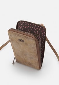 Portafoglio in pelle marrone con superficie texturizzata, chiusura con zip e fodera a pois rosa in contrasto. Presenta un logo discreto sul davanti.