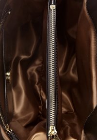 Schwarze Leder-Handtasche mit einem glatten, glänzenden braunen Innenfutter. Verfügt über einen goldenen Metallreißverschluss in der Mitte und ein strukturiertes Design.