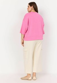 Roza oversized sweatshirt s kratkimi rokavi, v kombinaciji z bež širokimi trenirkami in bež balerinkami z teksturiranim vzorcem.
