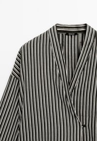 Veste style kimono à rayures verticales noires et blanches avec un devant croisé et une petite fermeture bouton sur le côté.