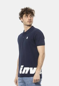 Polo shirt blu navy con colletto, maniche corte e stampa grafica bianca "inv" sul orlo. Presenta un piccolo emblema bianco sul petto.
