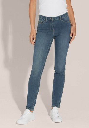 Blauwe skinny jeans van denim met een gemiddelde taillehoogte, met voorzakken en een ritssluitingen. Gecombineerd met witte sneakers op een lichte achtergrond.