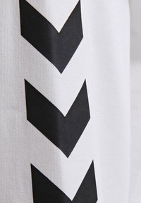 Trois grands chevrons noirs pointant vers le bas sont imprimés verticalement sur un fond en tissu blanc.