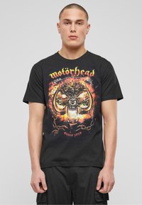 Černé bavlněné tričko s barevným grafickým potiskem lebky s rohy, plameny a nápisem "motörhead" nahoře ve žluté barvě. Obsahuje detail "od roku 1979".