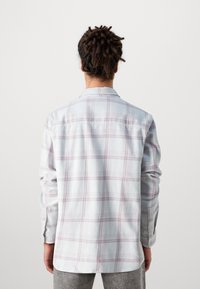 Light blue plaid shirt with pink and white lines, long sleeves, button-up front, and a curved hem, made from a soft, textured fabric.