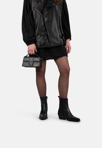 Chaqueta de cuero negra con cremalleras, una falda negra, medias transparentes y botas de tobillo negras con punta afilada y tacón apilado, combinadas con un bolso pequeño.