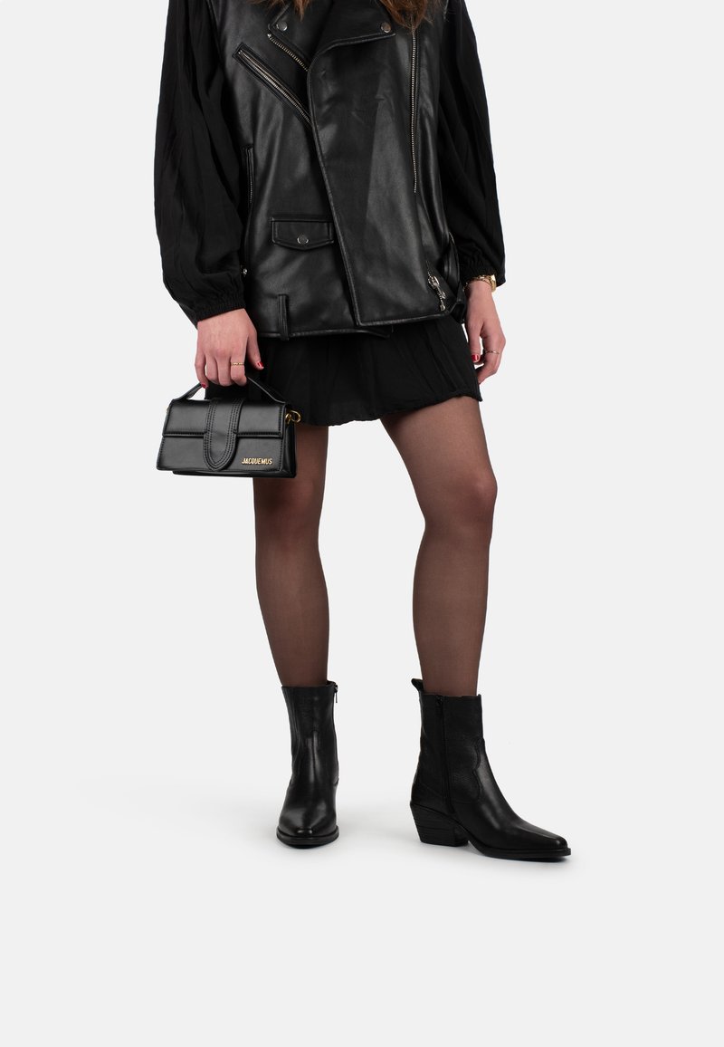 Chaqueta de cuero negra con cremalleras, una falda negra, medias transparentes y botas de tobillo negras con punta afilada y tacón apilado, combinadas con un bolso pequeño.