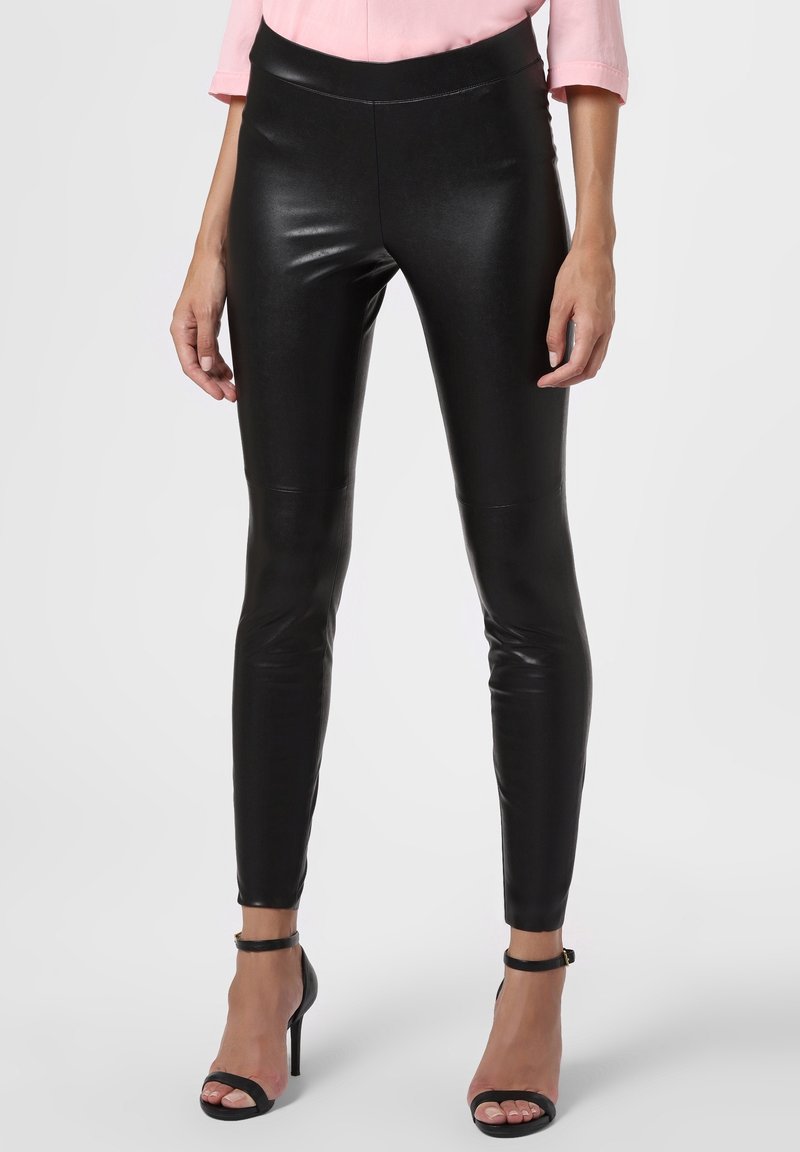 Svarta fusk läder leggings med hög midja, smal passform och slät yta. Bärs med svarta remsandaler med klack och en ljusrosa blus.