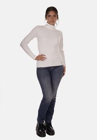 Maglione bianco a collo alto, aderente, con maniche lunghe; abbinato a jeans blu scuro e stivali neri con plateau. Design semplice, texture liscia.
