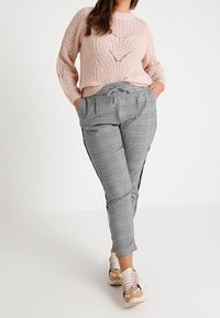 Pull rose clair en maille avec une coupe ample et un tissage ouvert, associé à un pantalon gris à carreaux avec taille à nouer et bandes latérales.
