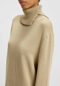 Beige gestrickter Rollkragensweater mit einem gerippten Kragen und Schulterdetails. Verfügt über lange Ärmel und einen lockeren Schnitt. Glatte Textur.