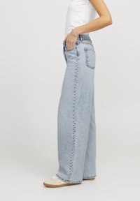 Jeans in denim azzurro a gamba larga con vita alta, caratterizzati da cuciture visibili e tasche laterali. Abbinati a sneakers beige.