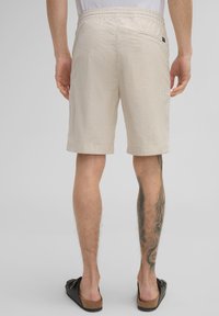 Beige gestreifte Shorts mit elastischem Bund und Gesäßtasche. Der Stoff ist leicht und hat eine glatte Textur, mit ordentlich gesäumten Kanten.