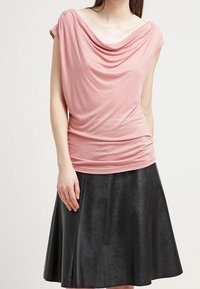 Růžový top s krátkými rukávy, zavěšený na ramenou, v kombinaci s černou koženou sukní ve tvaru A. Hladká textura látky, s nařasením kolem dekoltu.