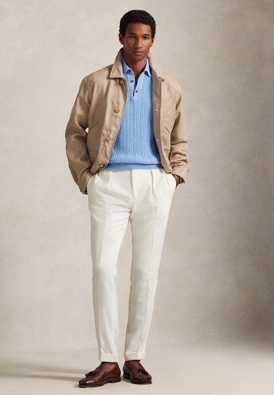 Beżowa lniana marynarka na jasnoniebieskim swetrze w warkocze, białe spodnie i brązowe skórzane buty. Prosty design, dopasowany krój.
