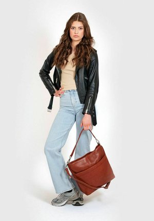 Sac à bandoulière en cuir marron avec une texture lisse, doté de deux poches avant et d'une longue bandoulière, associé à une veste en cuir noir et un jean bleu clair.