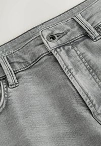 Szürke farmernadrág kopott hatással, gombos záródással és kontrasztos varrással. A derékrészen címke található márkajelzéssel.