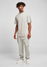 Lys grå t-skjorte med kort erme og en avslappet passform, kombinert med matchende joggebukser med lommer og snøring, iført hvite sneakers.