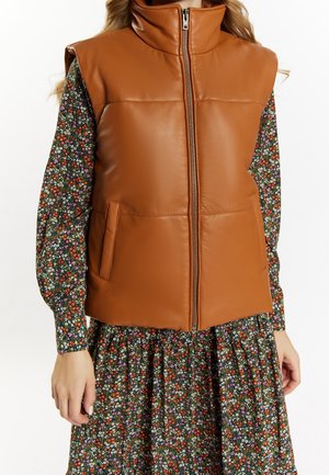 Veste en cuir matelassée marron avec fermeture éclair à l'avant portée sur une robe longue à manches longues à fleurs avec un mélange de petites fleurs orange, blanches et violettes.