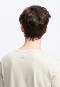 Licht beige katoenen t-shirt met een ronde halslijn en een subtiele grijze schaar borduursel op de achterkant nabij de halslijn.