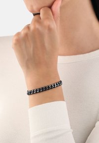 Bracciale a catena nero e argento con anelli intrecciati, caratterizzato da una superficie liscia e un design che si adatta strettamente attorno al polso.