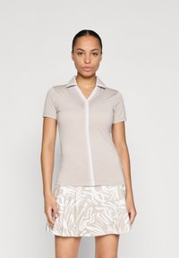 Μπεζ πόλο μπλούζα κοντό μανίκι με μπροστινό φερμουάρ, που διαθέτει λευκό γιακά και λεπτομέρειες αντίθεσης. Συνδυασμένη με μια φλοράλ φούστα σε μπεζ και λευκό.