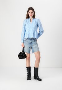 Blusa peplum azzurro chiaro con dettagli a occhiello, abbinata a pantaloni shorts in denim sfrangiati. Stivali neri al ginocchio e una piccola borsa floreale completano il look.