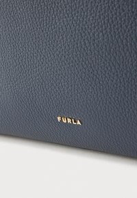 Tamnoplava kožna torba s teksturiranom površinom i zlatnim detaljima. Na boku je istaknuto zlatno "FURLA" logotip.
