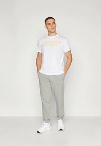 Calças de moletom cinzentas e uma t-shirt branca com gráficos amarelos. O conjunto apresenta um corte descontraído e material de algodão suave, combinado com ténis brancos.