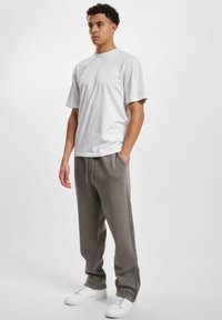 Hvit bomull t-skjorte kombinert med grå joggebukser med snøring og sidelommer. Modellen bruker hvite joggesko. Enkelt og avslappet design.