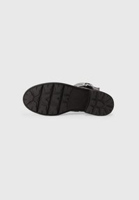 Black shoe sole featuring a rugged design with deep treads for traction. Made of rubber, it includes a textured surface and embossed branding.