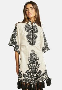 Abito ricamato in lino crema con intricati motivi floreali neri, maniche corte, colletto e frange nere all'orlo.