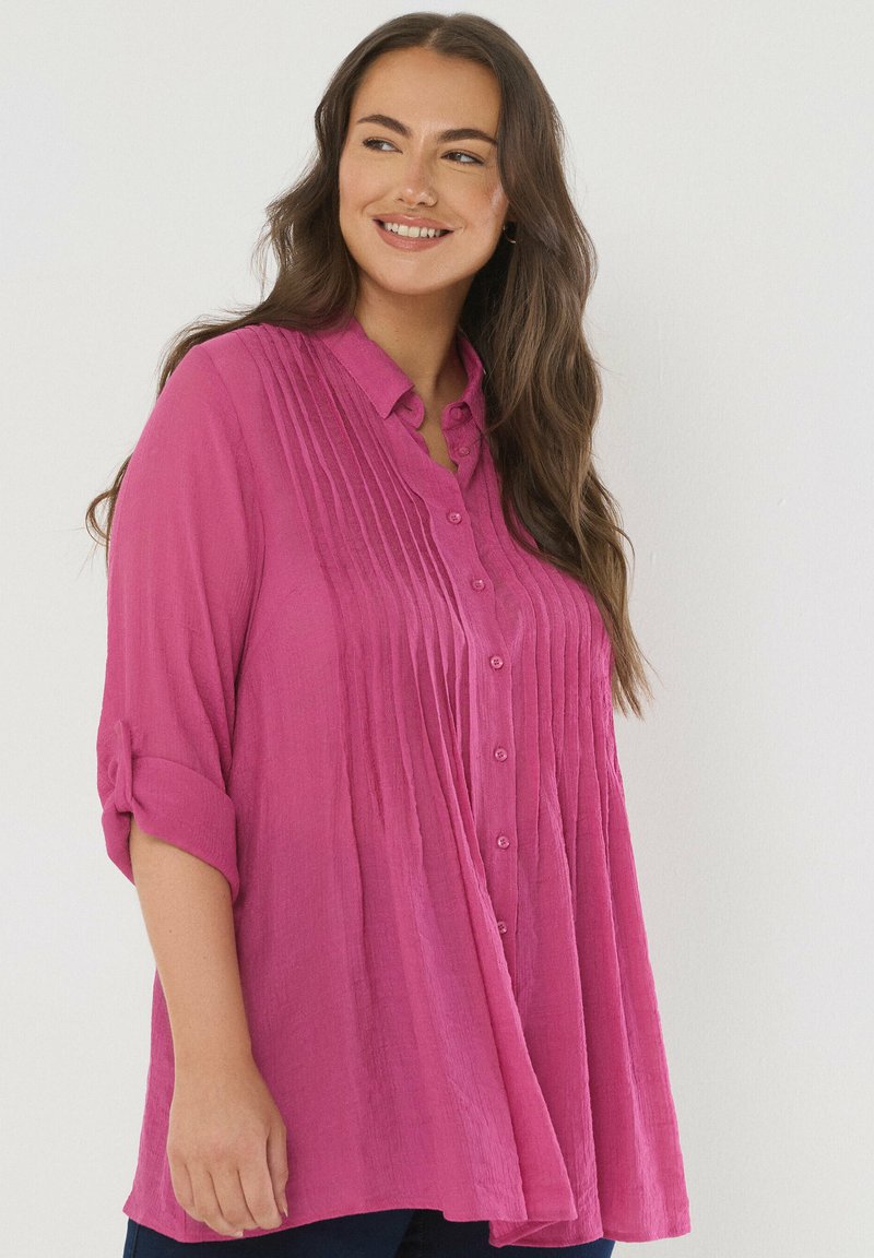 Blusa de un brillante color rosa, con botones y textura plizada, mangas enrollables y un corte relajado. Confeccionada con una tela ligera para mayor comodidad.