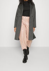 Grå uldfrakke med en dobbeltbreasted design, sort ribbet top og lyserøde faux læder bukser med vidde. Sorte snørebånd støvler fuldender outfittet.