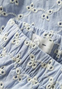 Svetlo modra tkanina z belimi vezenimi vzorci cvetja; elastika v pasu z gumbi za zapiranje; mehka, teksturirana bombažna tkanina.