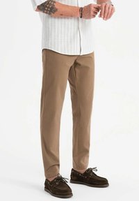 Pantalons beiges à coupe droite, en tissu léger, associés à des chaussures marron foncé à lacets. Chemise blanche rayée au-dessus.