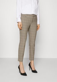 Beige, rutmönstrade byxor med slim fit, ankellängd och en slät textur, i kombination med svarta, spetsiga högklackade skor.