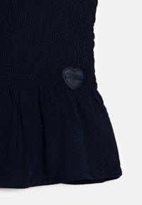 Tmavě modrý top z texturované látky, s nařaseným živůtkem, volánkovým lemem a srdcovým tmavě modrým gumovým logem.