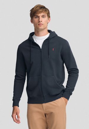 Felpa con zip di colore blu navy realizzata in tessuto morbido, con tasca a marsupio e cordini, e un piccolo logo rosso sul petto.
