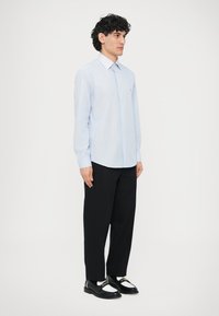 Jasnoniebieska koszula w paski z długim rękawem i kołnierzykiem na guziki, zestawiona z czarnymi spodniami i czarnymi mokasynami, prezentowana na modelu.