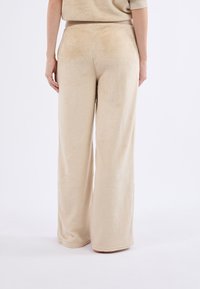 Pantalons beige à jambes larges en tissu doux et pelucheux, avec une taille haute et des coutures propres et simples. La texture semble lisse et veloutée.