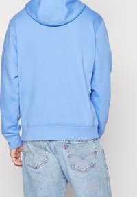 Ljusblå hoodie med dragsko i huvan, mjuk textur, ribbade ärmslut och nederkant; matchad med blekta blå denimjeans med bakfickor.