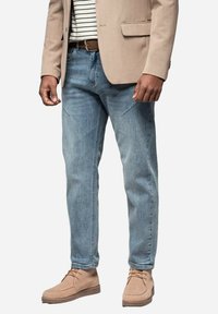 Jeans de mezclilla azul claro con un corte recto, combinados con un blazer beige y zapatos de ante color marrón claro. Presenta una textura sutil y un diseño clásico.