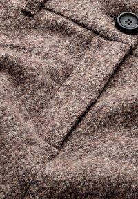 Tissu de manteau en laine texturé marron et beige avec un bouton noir à quatre trous et une couture détaillée sur le col.