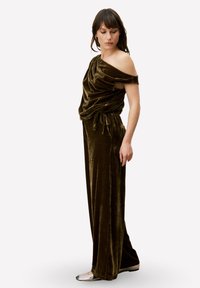 Olijfgroene velvet jumpsuit met een gedrapeerd, off-shoulder ontwerp, een ceintuur die de taille accentueert en wijde broekspijpen. Kenmerkt zich door een zachte textuur en glanzende accenten.