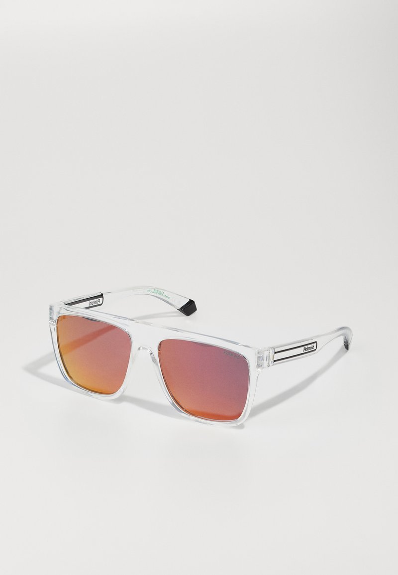 Lunettes de soleil rectangulaires transparentes avec des verres dégradés orange, monture transparente et embouts de branches noirs. Détails argentés sur les côtés.