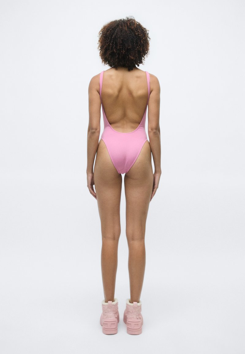 Roze badpak met een lage rugontwerp. Draag het met luchtige roze enkellaarsjes. Gladde textuur, vormgevende snit, minimalistische stijl.